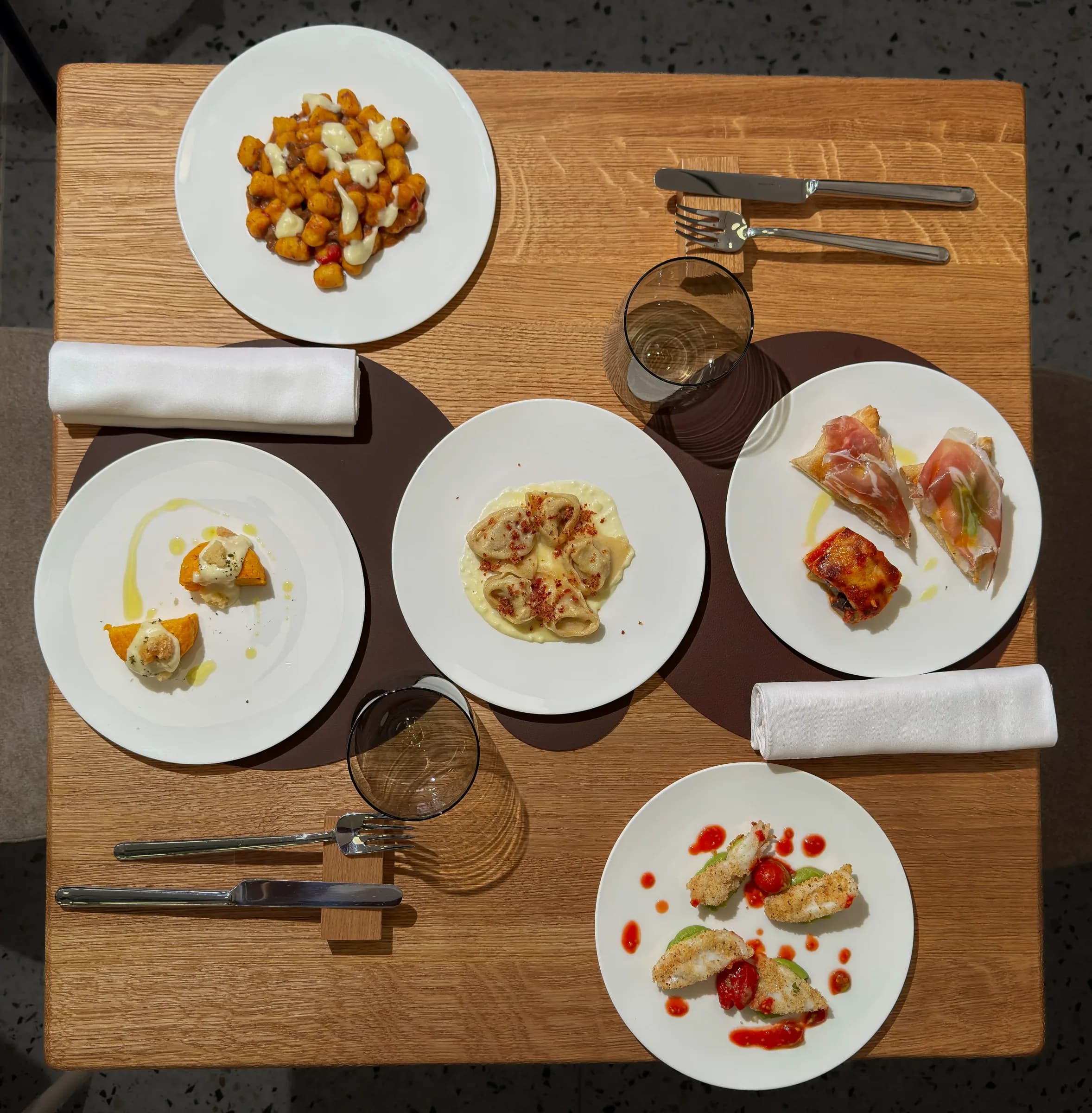 Vista dall'alto di un tavolo per due con cinque piattini dell'aperitivo, calice di vino e tovaglioli, Materia Osteria Contemporanea