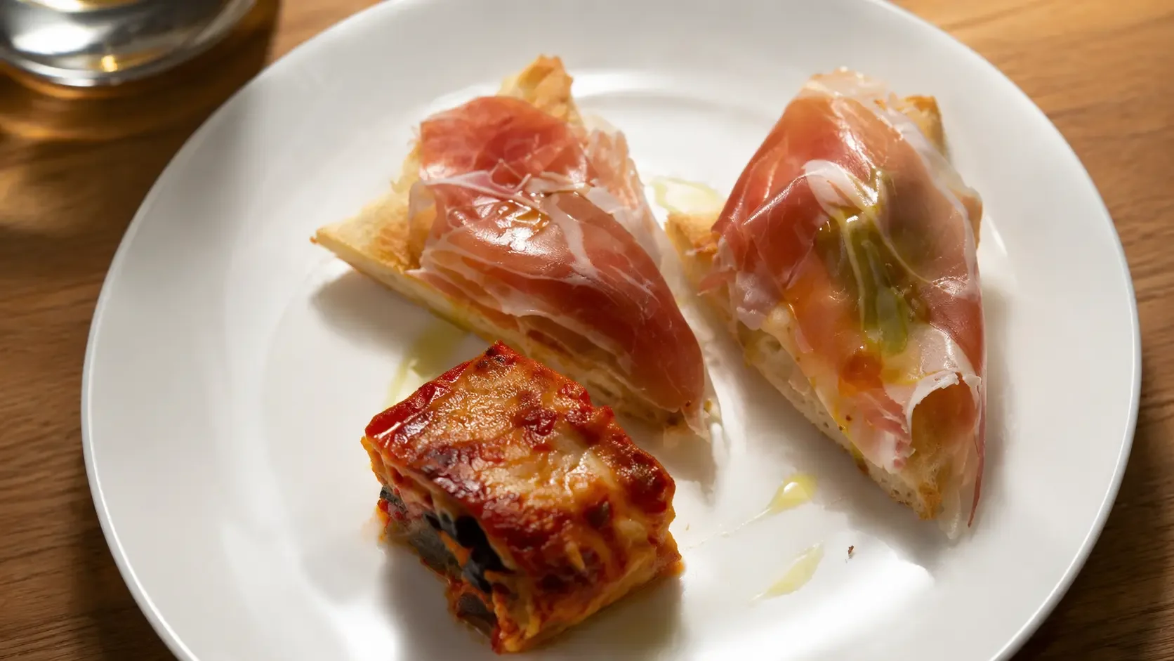 Focaccia con prosciutto crudo e cubo di parmigiana alla siciliana su piatto bianco, piattino dell'aperitivo di Materia