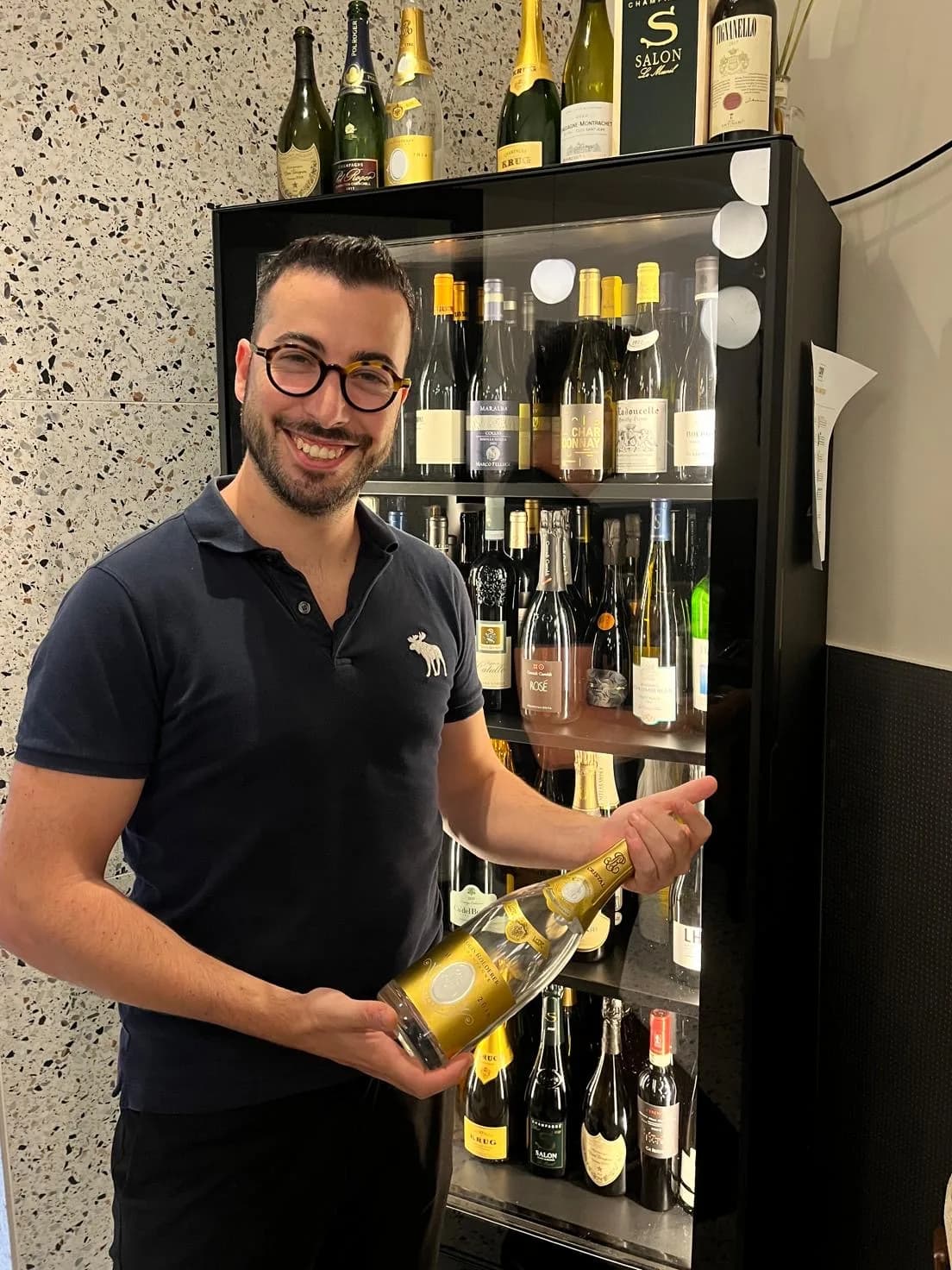 Mattia Raiti con una bottiglia di vino davanti alla cantinetta di Materia