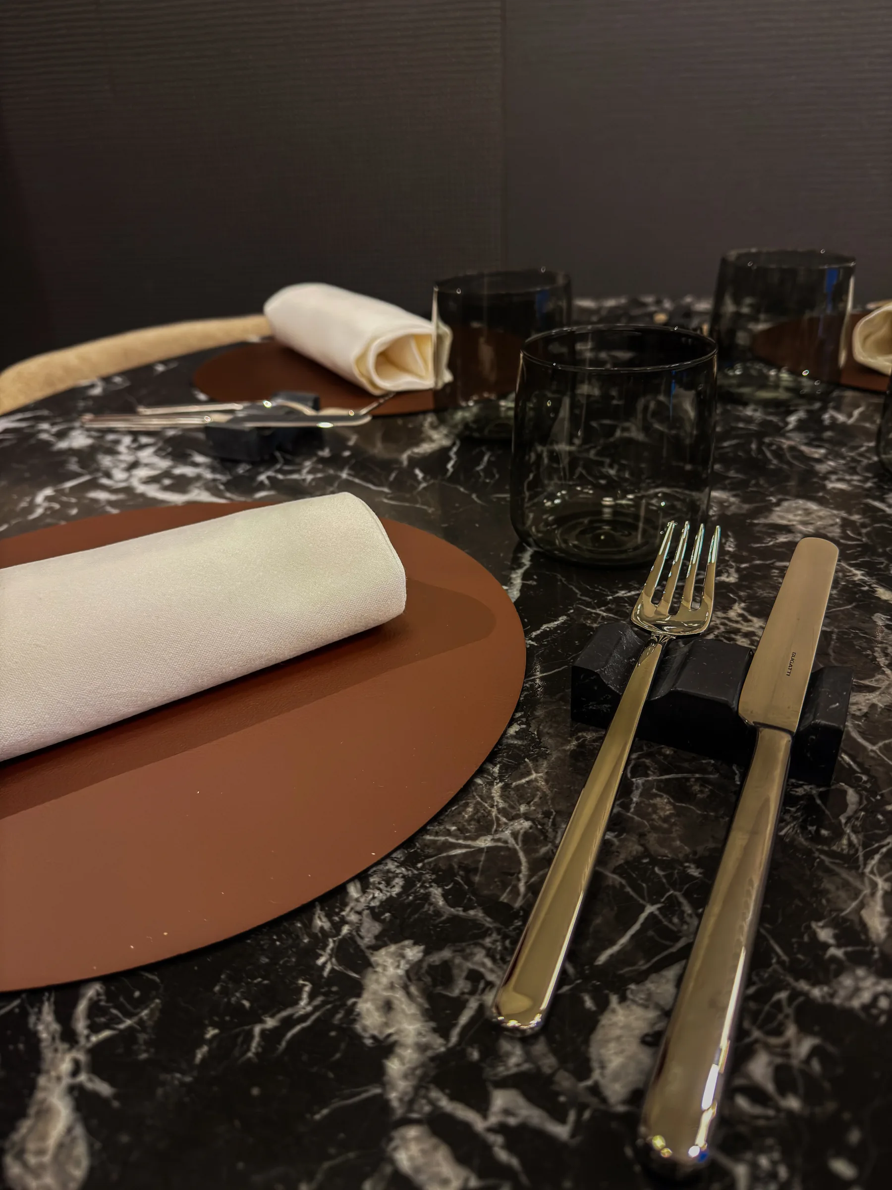 Dettaglio ravvicinato della mise en place su marmo nero, tovagliolo bianco e sottopiatto bordeaux, Materia Osteria Contemporanea